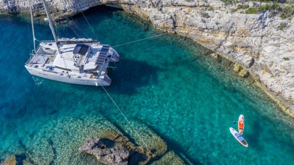 Catamaran Marla anchored in crystal-clear waters with water sports equipment nearby.